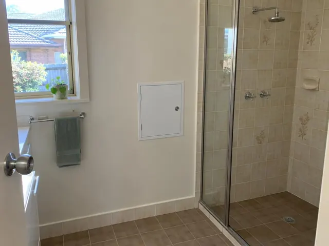 Bathroom wall with a small access panel beside a tiled shower and window in Kingswood
